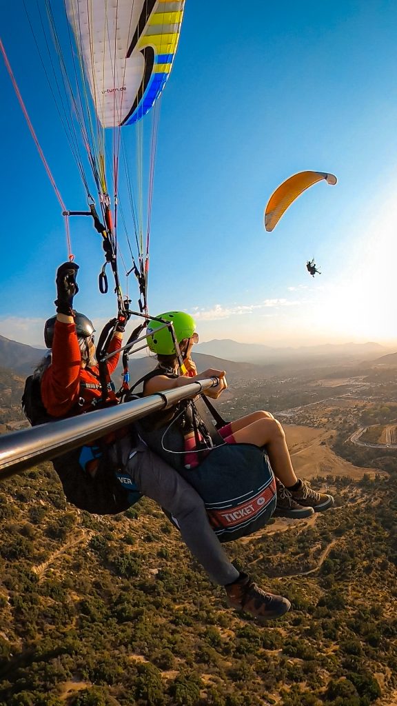 Woman looking off towards another parachute in the distance, high above the ground while the paragliding guide controls the parachute