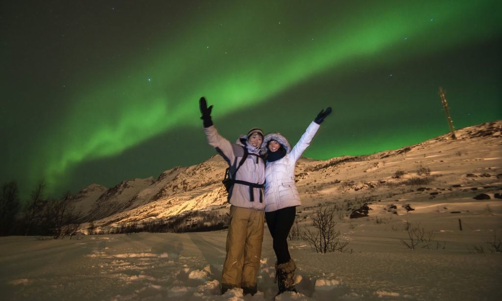 A man and woman under the green Aurora Borealis in Tromsø, Norway