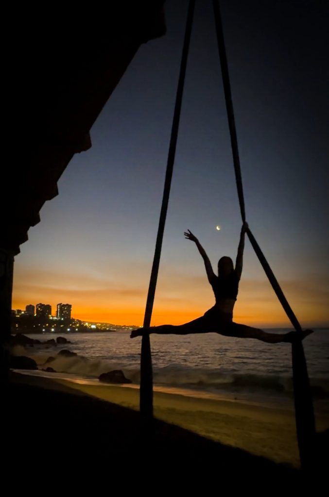 Woman doing the splits on aerial silks on the beach at sunset in Viña del Mar Chile