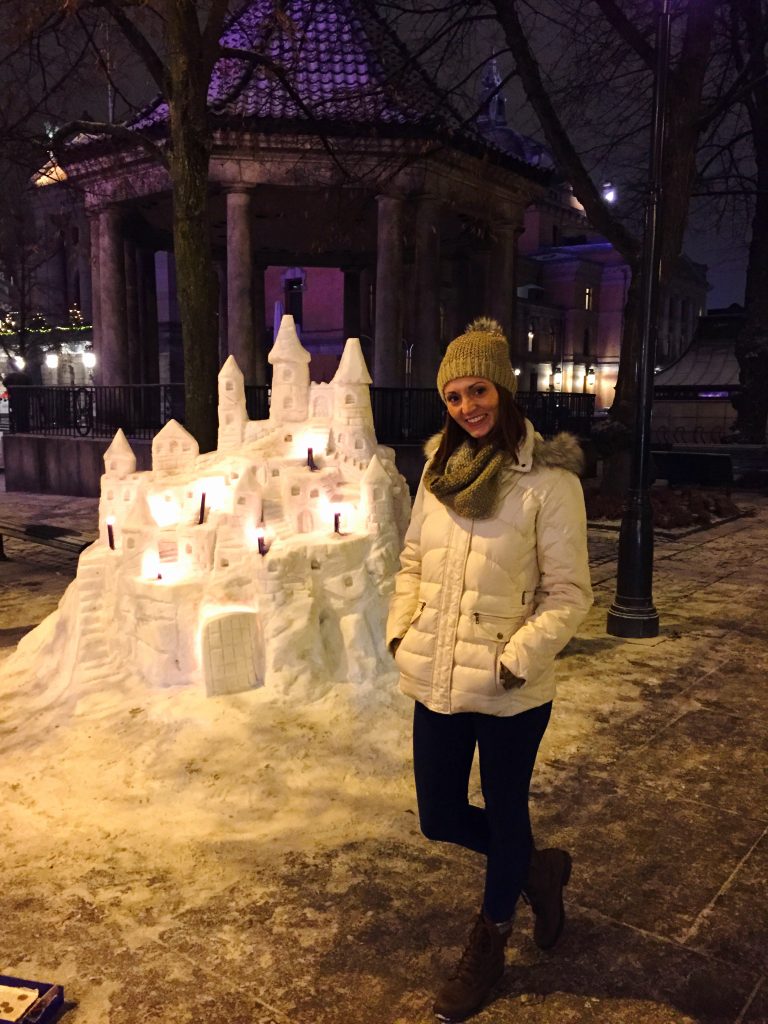 A woman standing in front of a large castle made of snow with candles on it at night