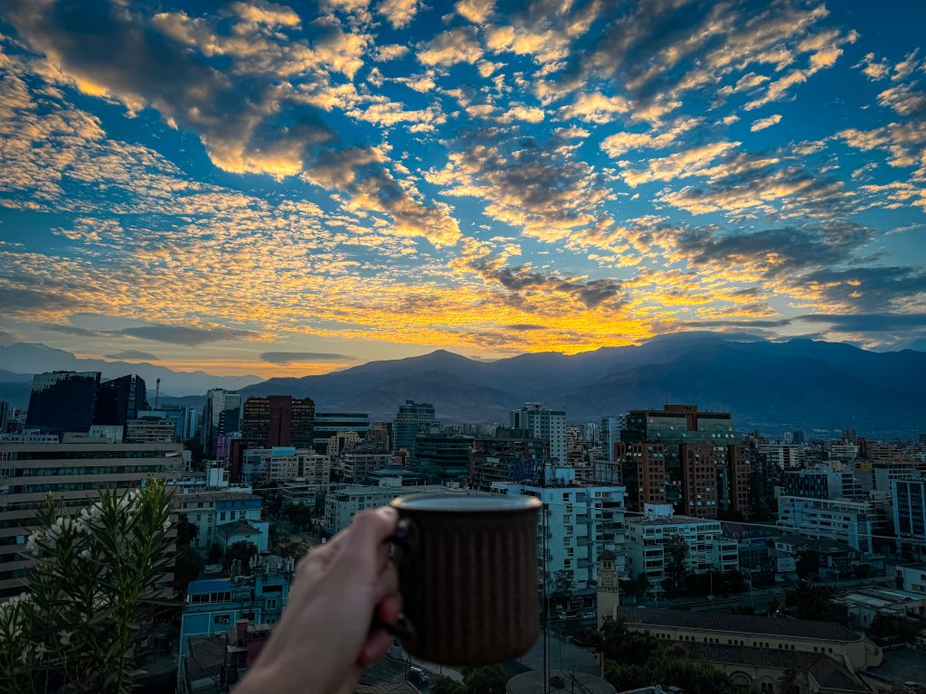 hand holding cup of coffee in santiago at sunrise over the Andes mountains