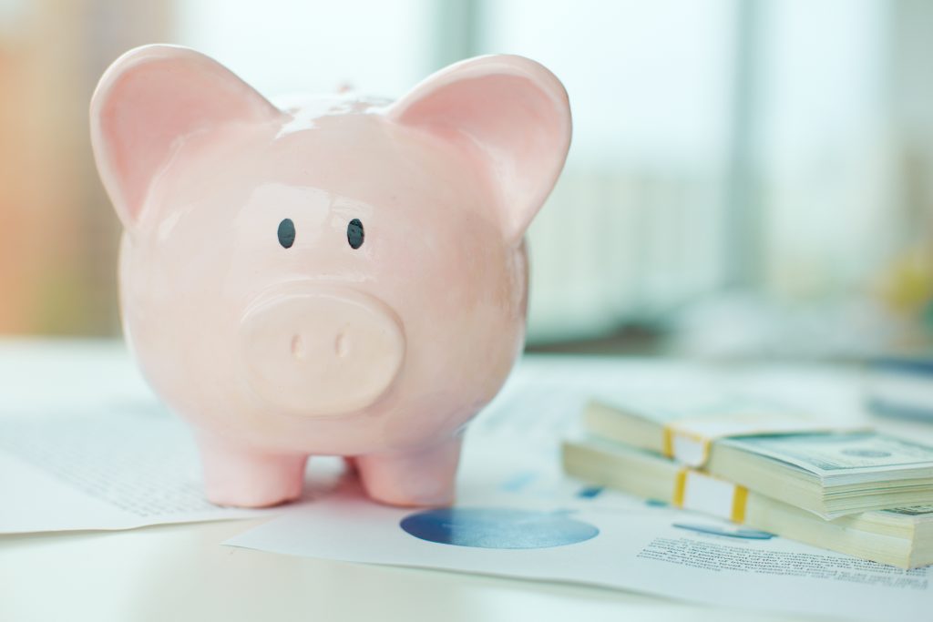 pink piggy bank with a stack of dollars to save for travel
