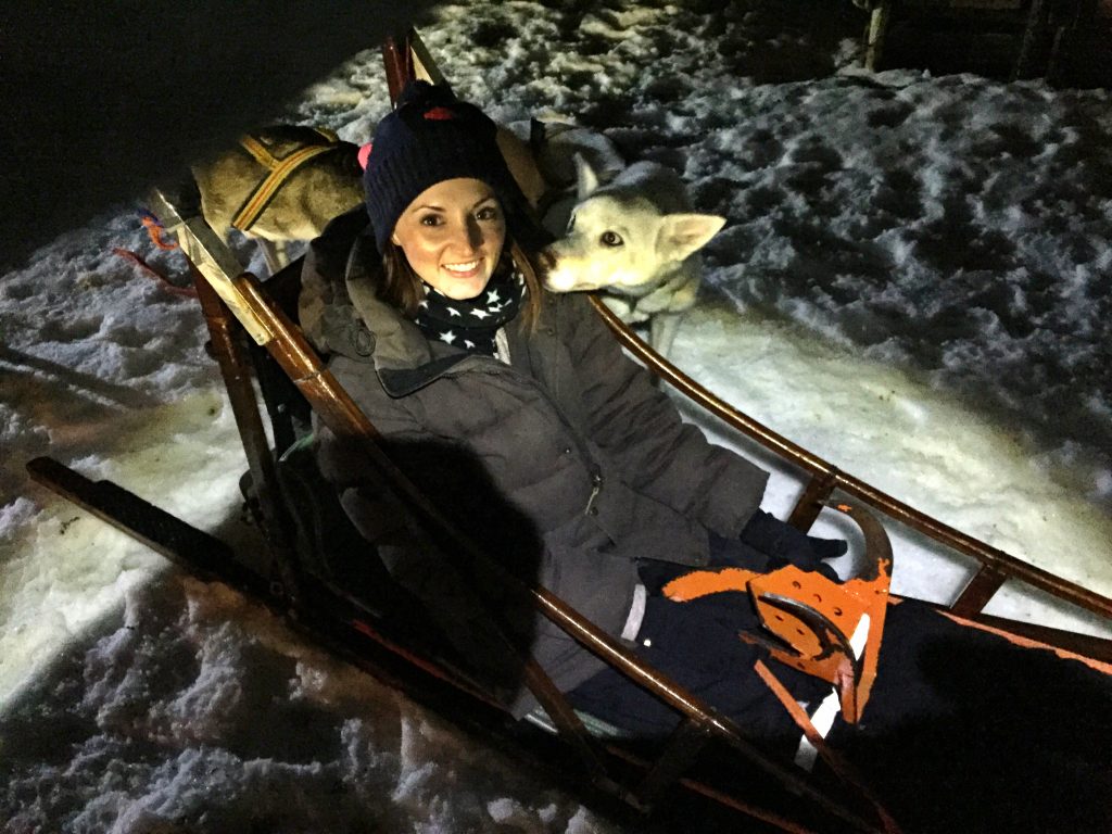 Woman sitting in a dog sled with a husky looking at her