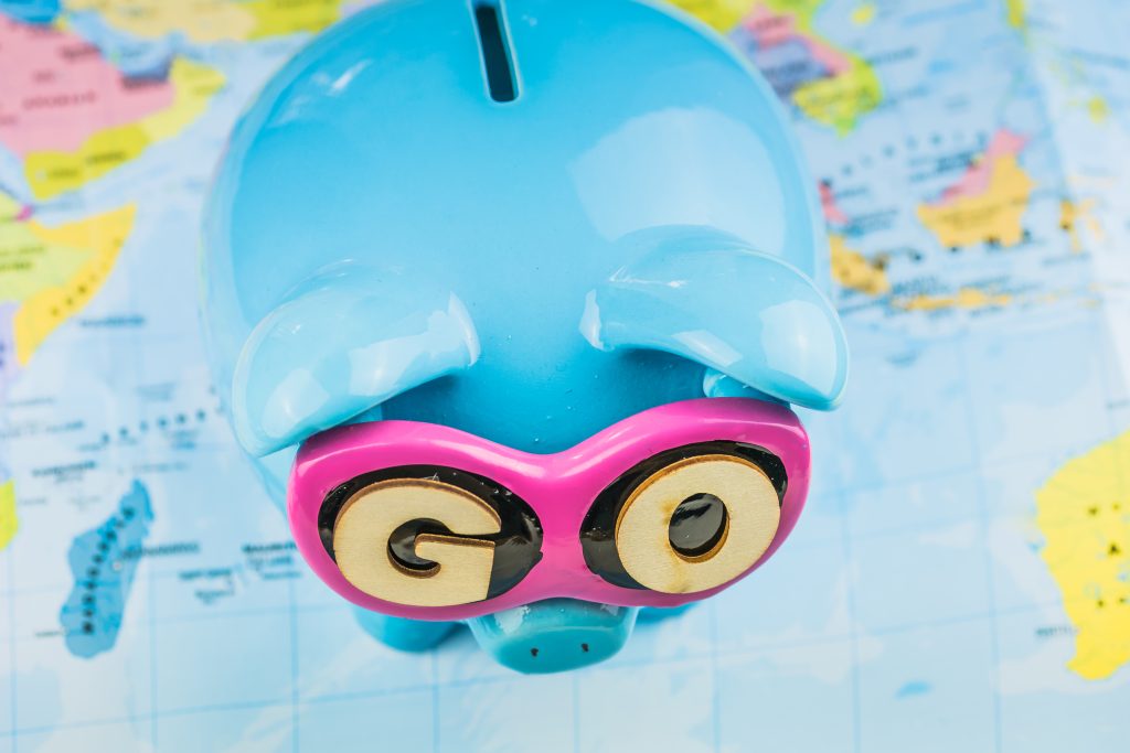 A piggy bank wearing googles that say "Go" standing on a map of the world