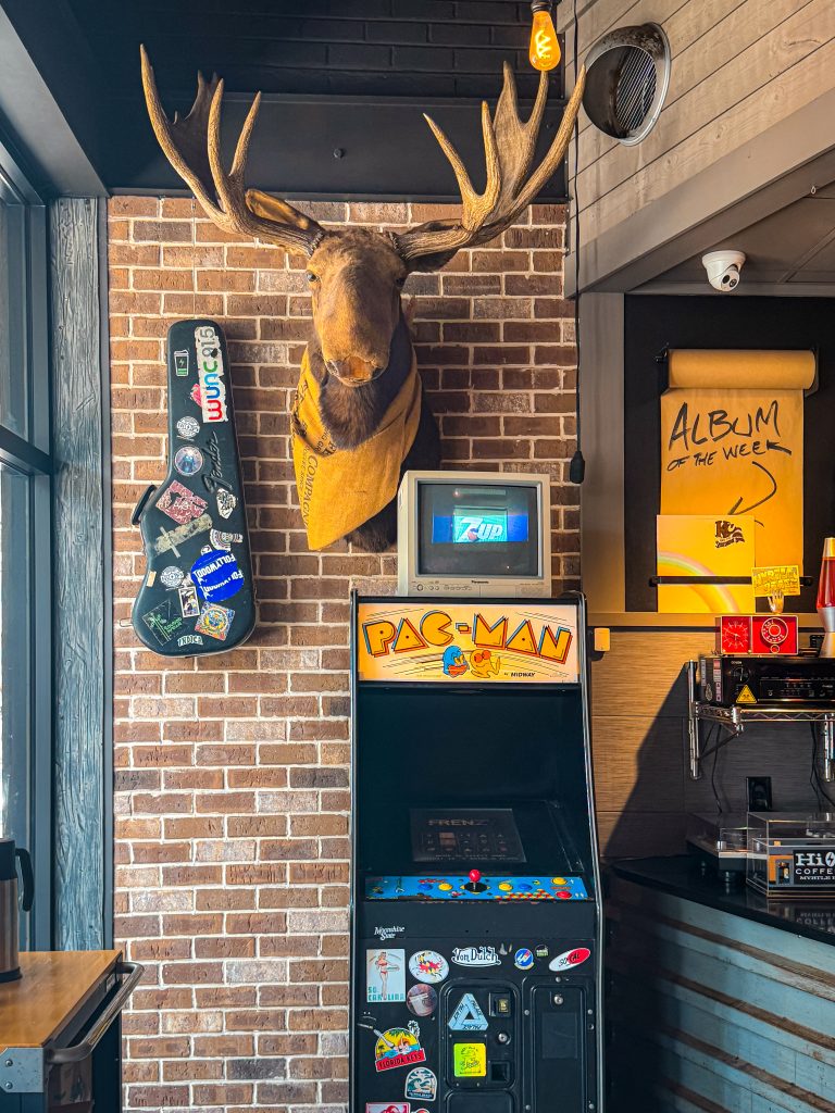 Brick wall with stickered guitar case, moose head, and pac-man arcade game
