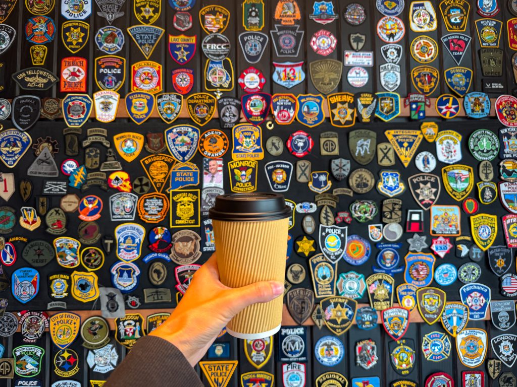 Coffee cup held in front of wall of military badges at Black Rifle Coffee Company