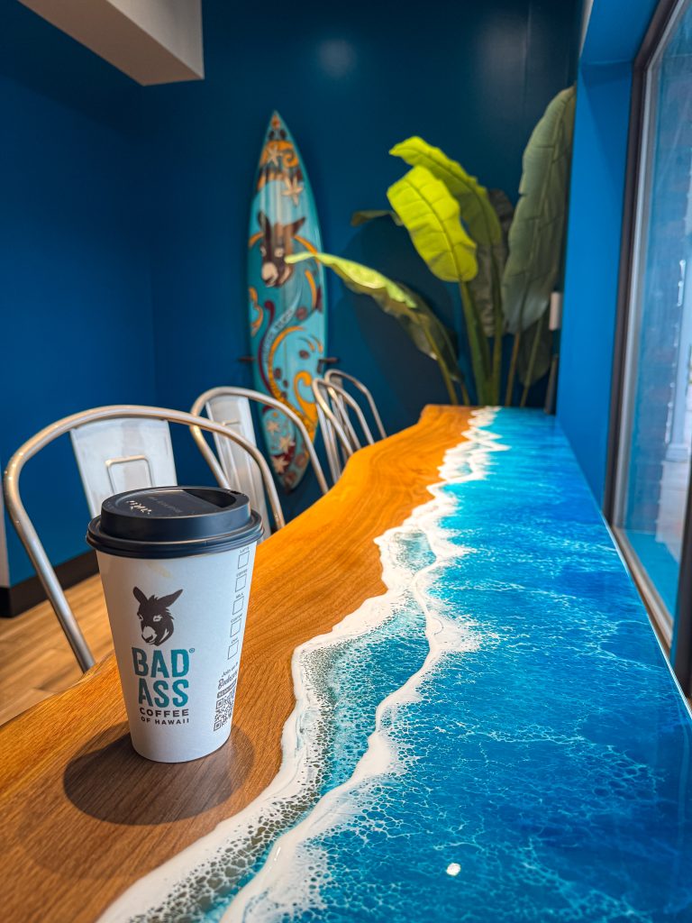 Coffee on a table that looks like a beach with a surfboard on the wall behind