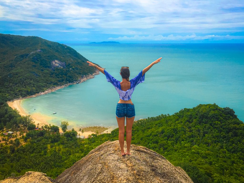 Woman standing with arms outstretched at the top of a cliff overlooking the turquoise water