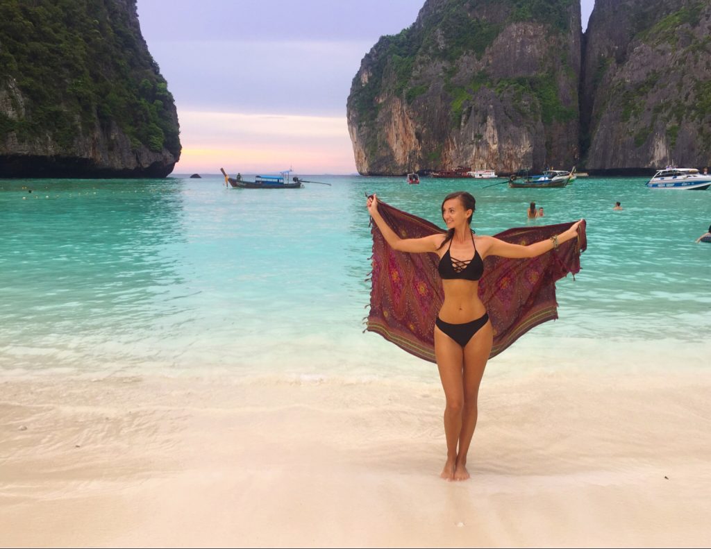 Woman standing in Maya Bay at sunset with beach and cliffs behind her