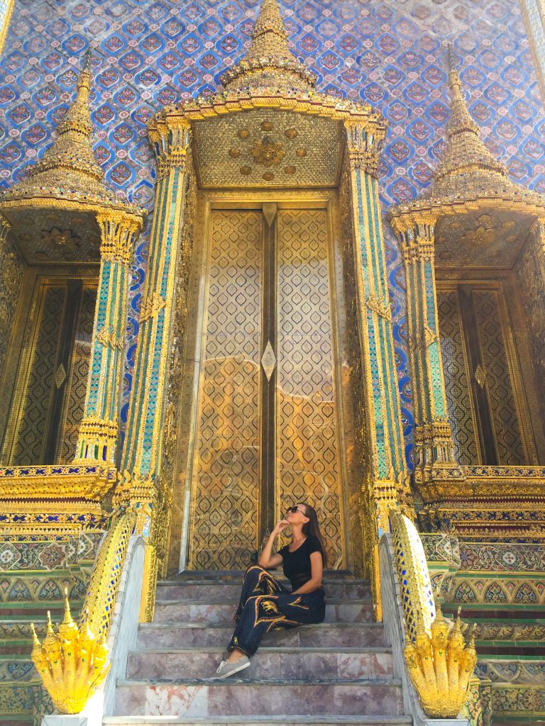 Woman sitting on Grand Palace steps in front of ornate, gold doors