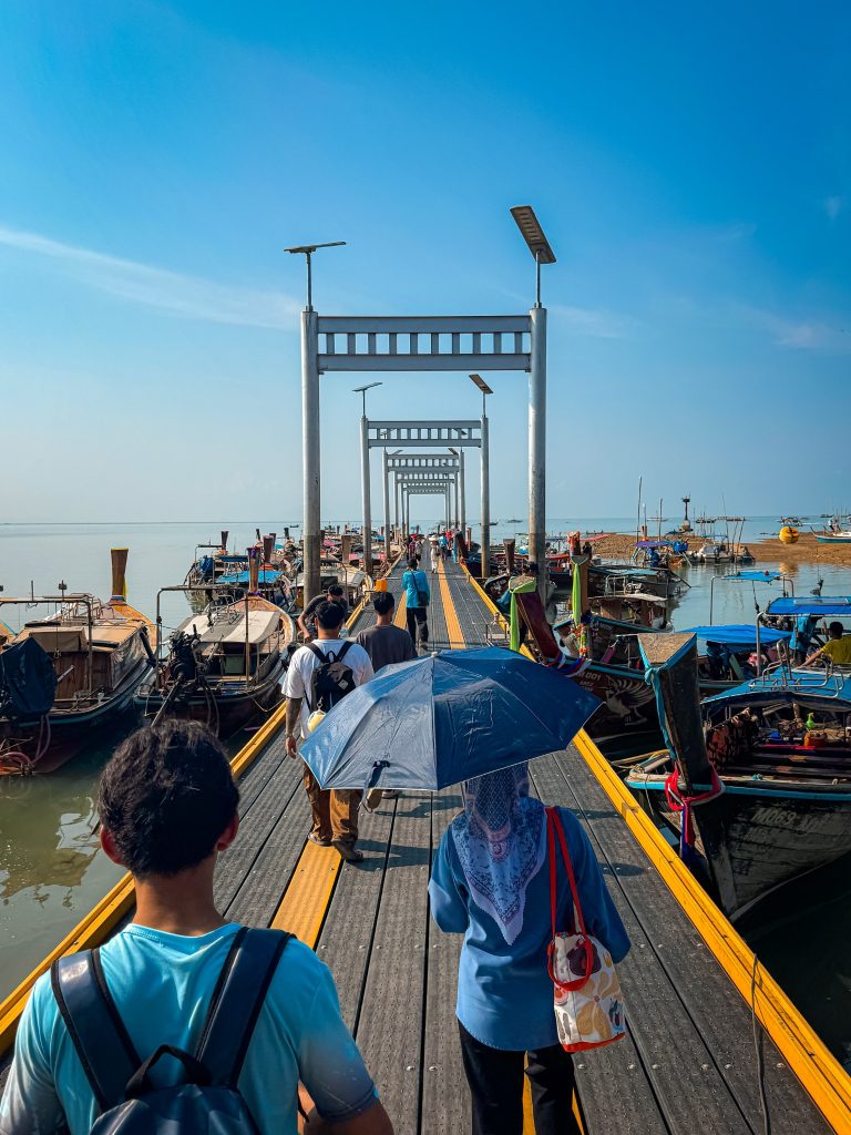Passengers walking along Ao Nam Mao Pier between rows of traditional longtail boats.