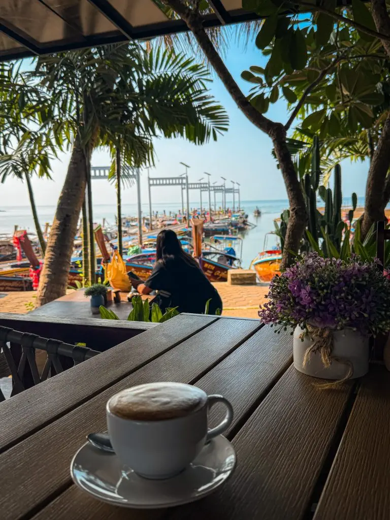 Cup of coffee overlooking colorful longtail boats from D’oasis Cafe at Ao Nam Mao Pier.