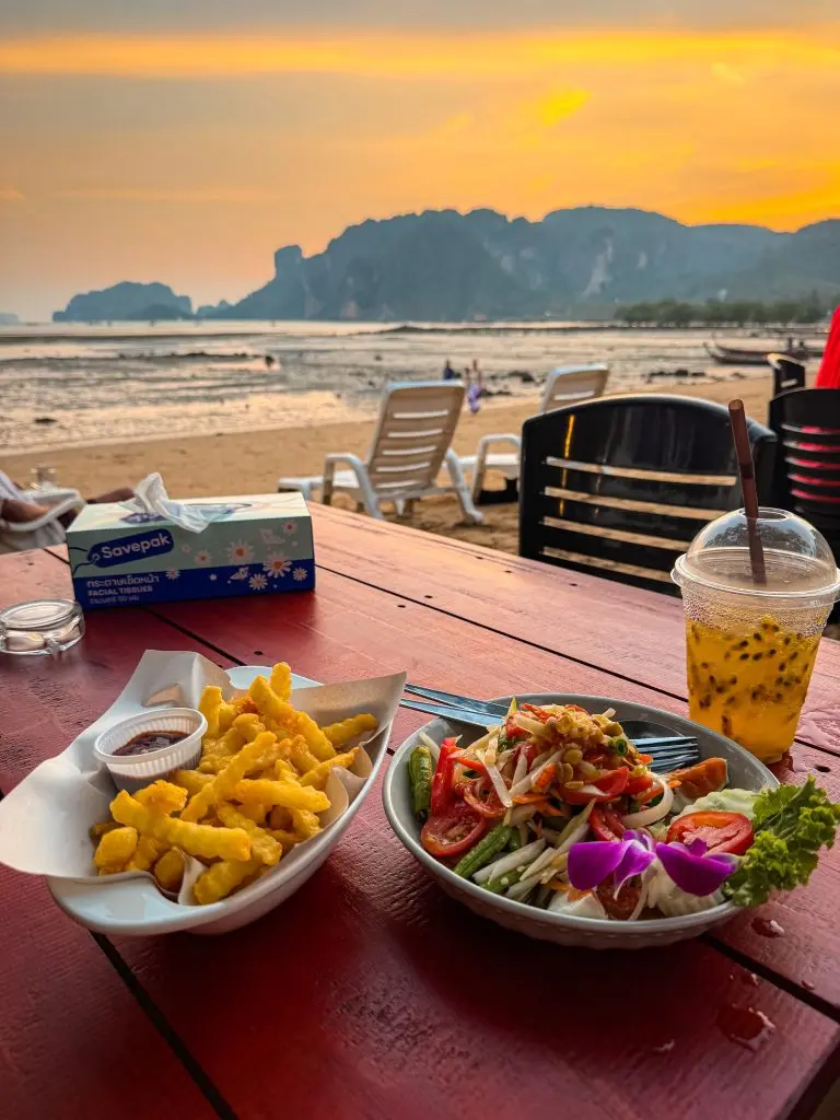 Papaya salad, fries, and a passion fruit drink served at Joy Thai Food with a sunset beach view.