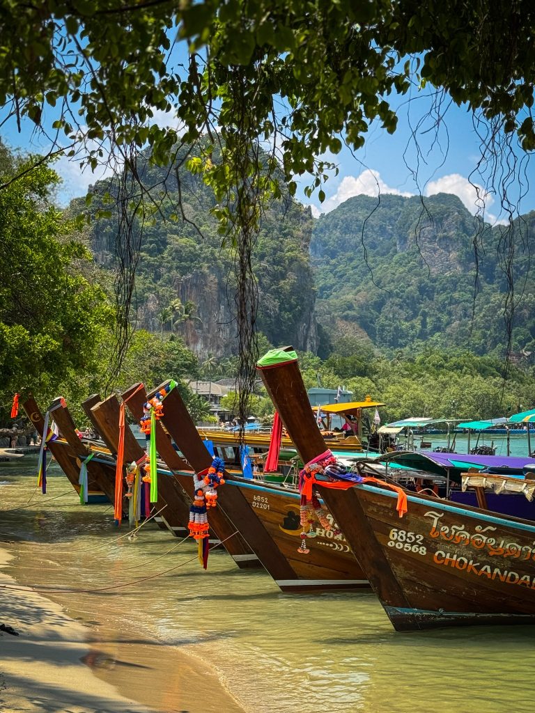 Colorful traditional longtail boats lined up along Railay Beach beneath limestone mountains.