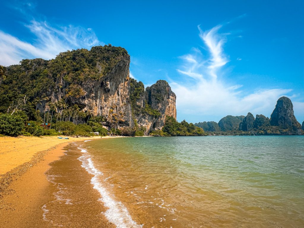 Quiet stretch of Railay Beach with gentle waves and limestone mountains along the coast.