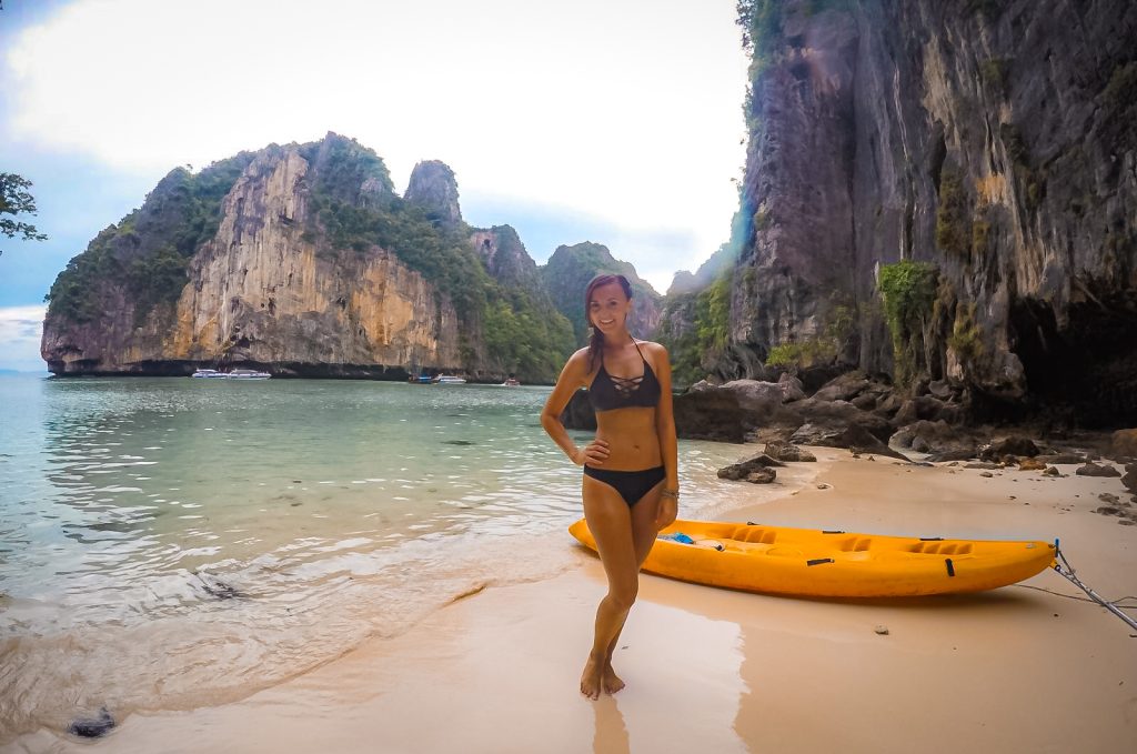 Woman standing beside a yellow kayak on a secluded Railay Beach surrounded by limestone cliffs.