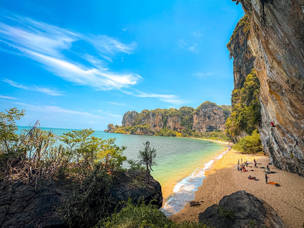 Elevated view of Tonsai Beach, with rock climbers, turquoise water, and limestone cliffs from a rocky cliffside path.
