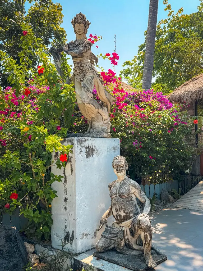 Weathered Thai statues among bright tropical flowers in the Villa Cha-Cha Krabi garden.