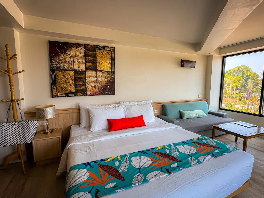 King bed, sofa, tropical bed runner, and large windows in an ocean-view room at Villa Cha-Cha Krabi.