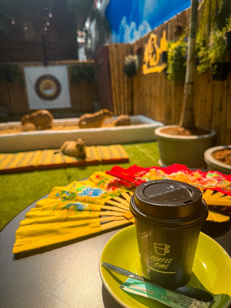 Cup of coffee with colorful fans and capybaras relaxing in the background at Capybara Cafe Thailand.