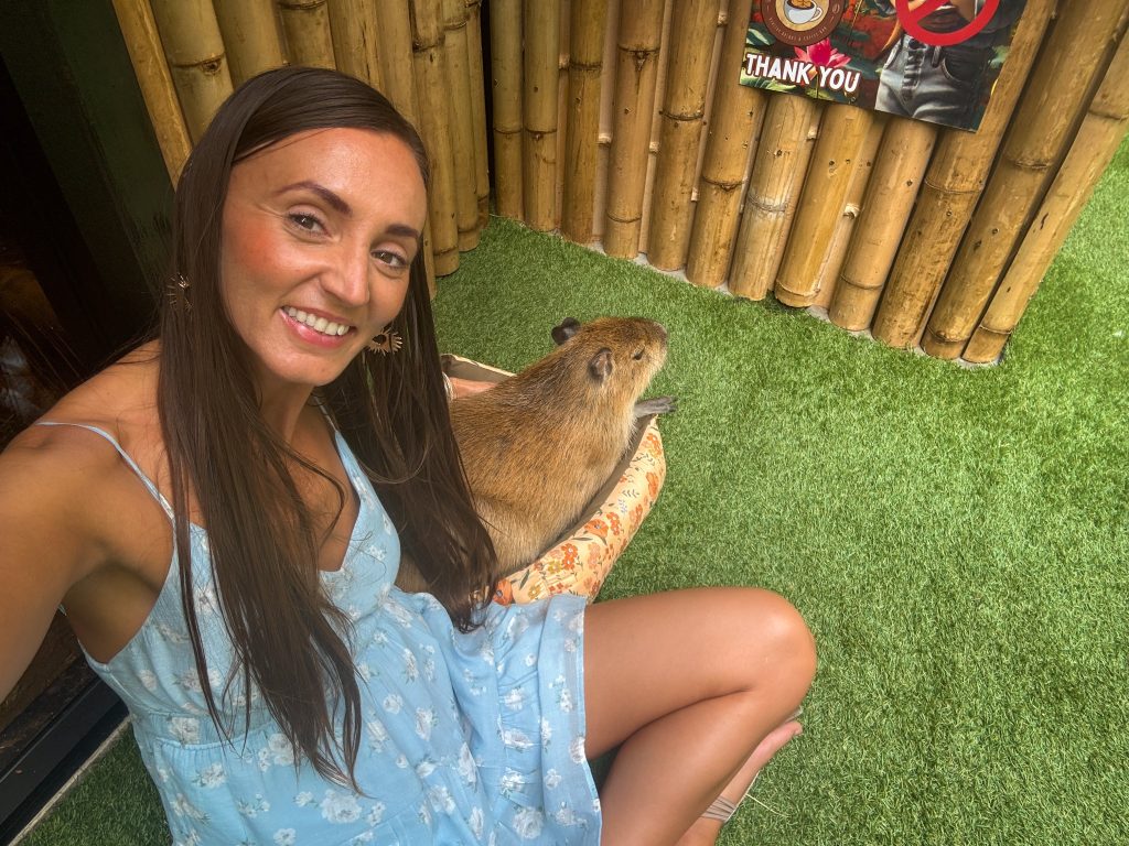 Woman taking a selfie beside a capybara relaxing in a small bed at Capybara Cafe Thailand.