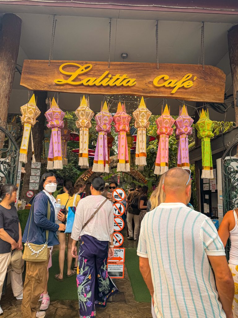 Entrance to Lalitta Cafe Chiang Rai with a wooden cafe sign and colorful hanging lanterns.