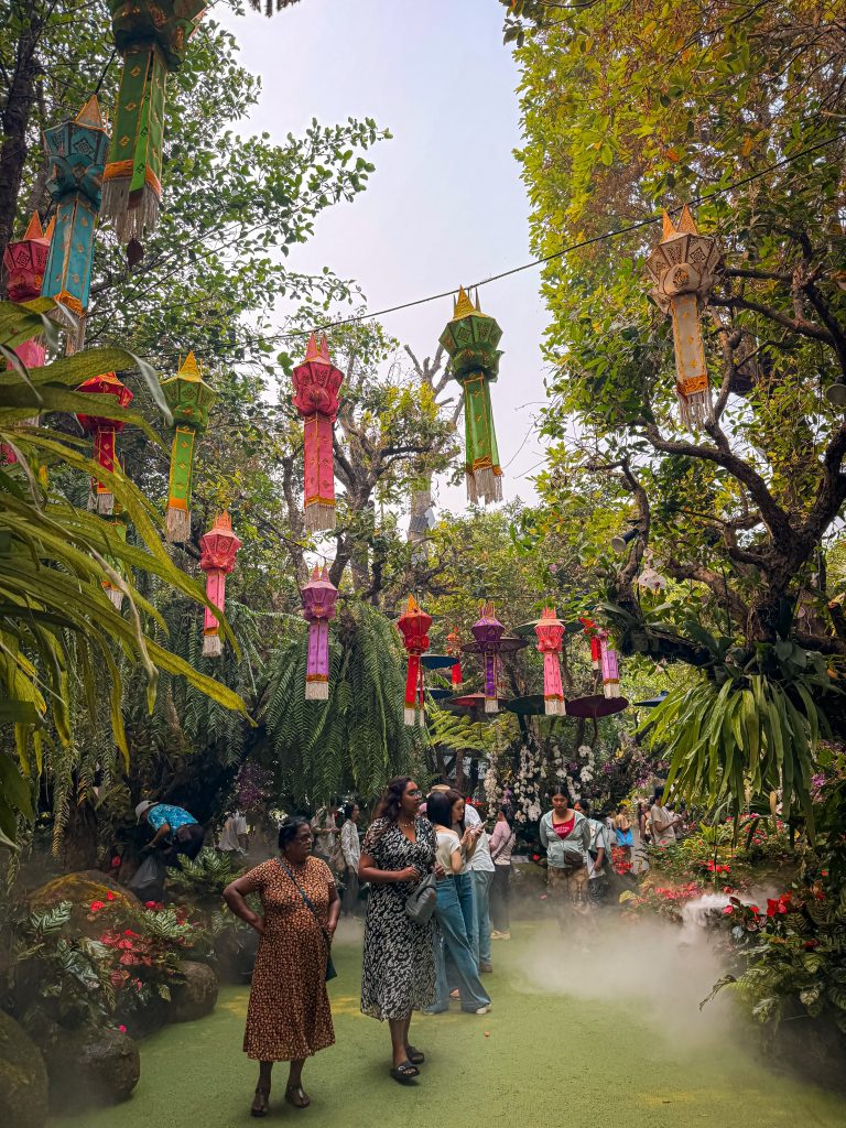 Colorful traditional lanterns hanging above visitors in the tropical garden at Lalitta Cafe Chiang Rai.