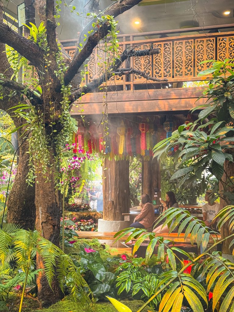 Wooden seating area built among trees, ferns, flowers, and hanging lanterns at Lalitta Cafe Chiang Rai.