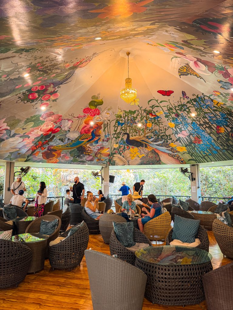 Cafe seating beneath an elaborate ceiling mural featuring peacocks, butterflies, and flowers at Lalitta Cafe Chiang Rai.