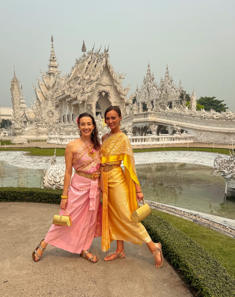 Two women wearing pink and gold traditional Thai dresses beside the pond at the White Temple in Chiang Rai.
