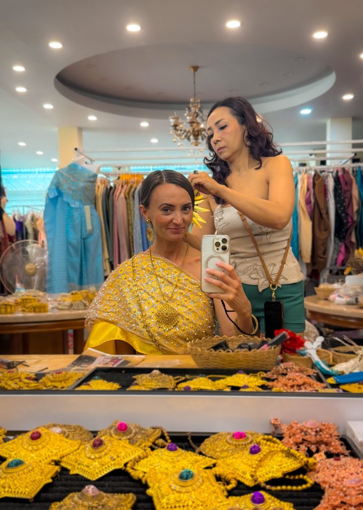 Woman having her hair styled with a yellow flower while wearing a traditional Thai dress at a Chiang Rai rental shop.