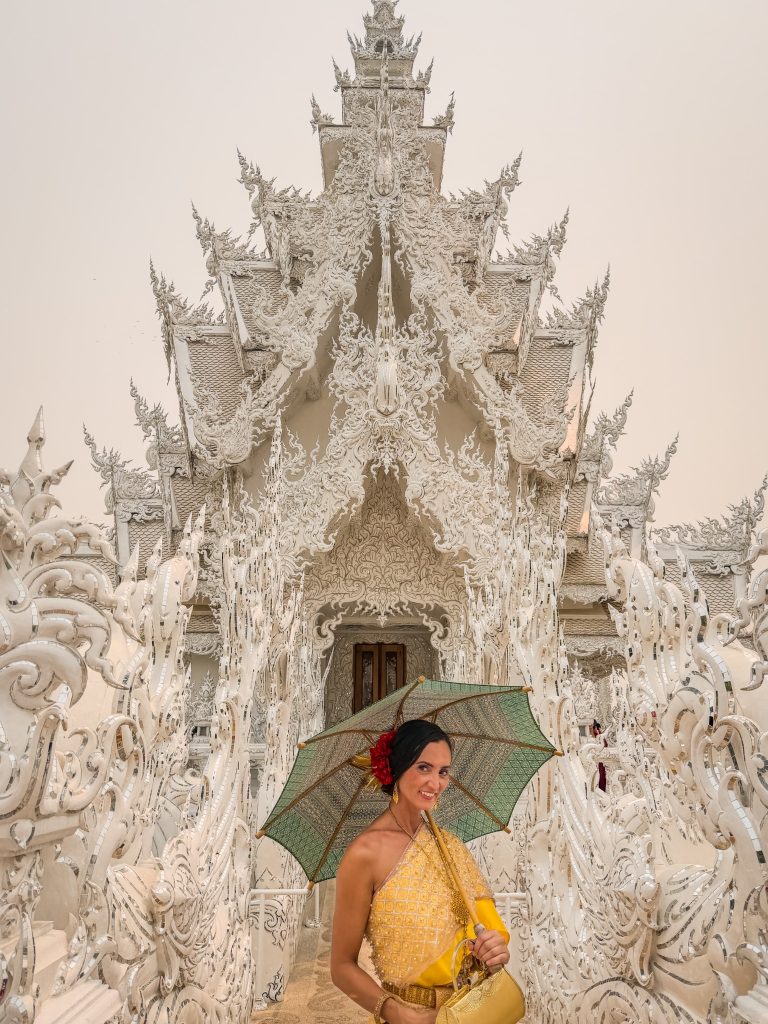 Woman in a gold traditional Thai dress holding a green parasol on the ornate bridge at the White Temple.