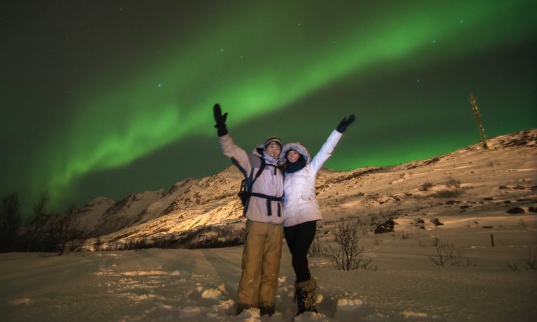 A man and woman under the green Aurora Borealis in Tromsø, Norway