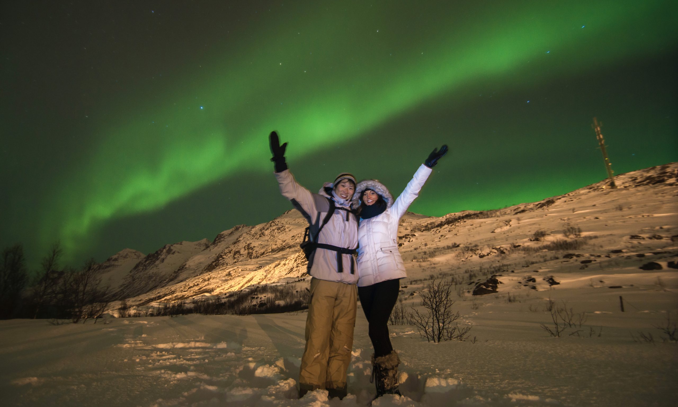 A man and woman under the green Aurora Borealis in Tromsø, Norway