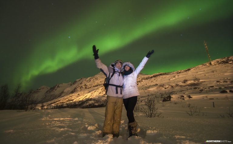 A man and woman under the green Aurora Borealis in Tromsø, Norway