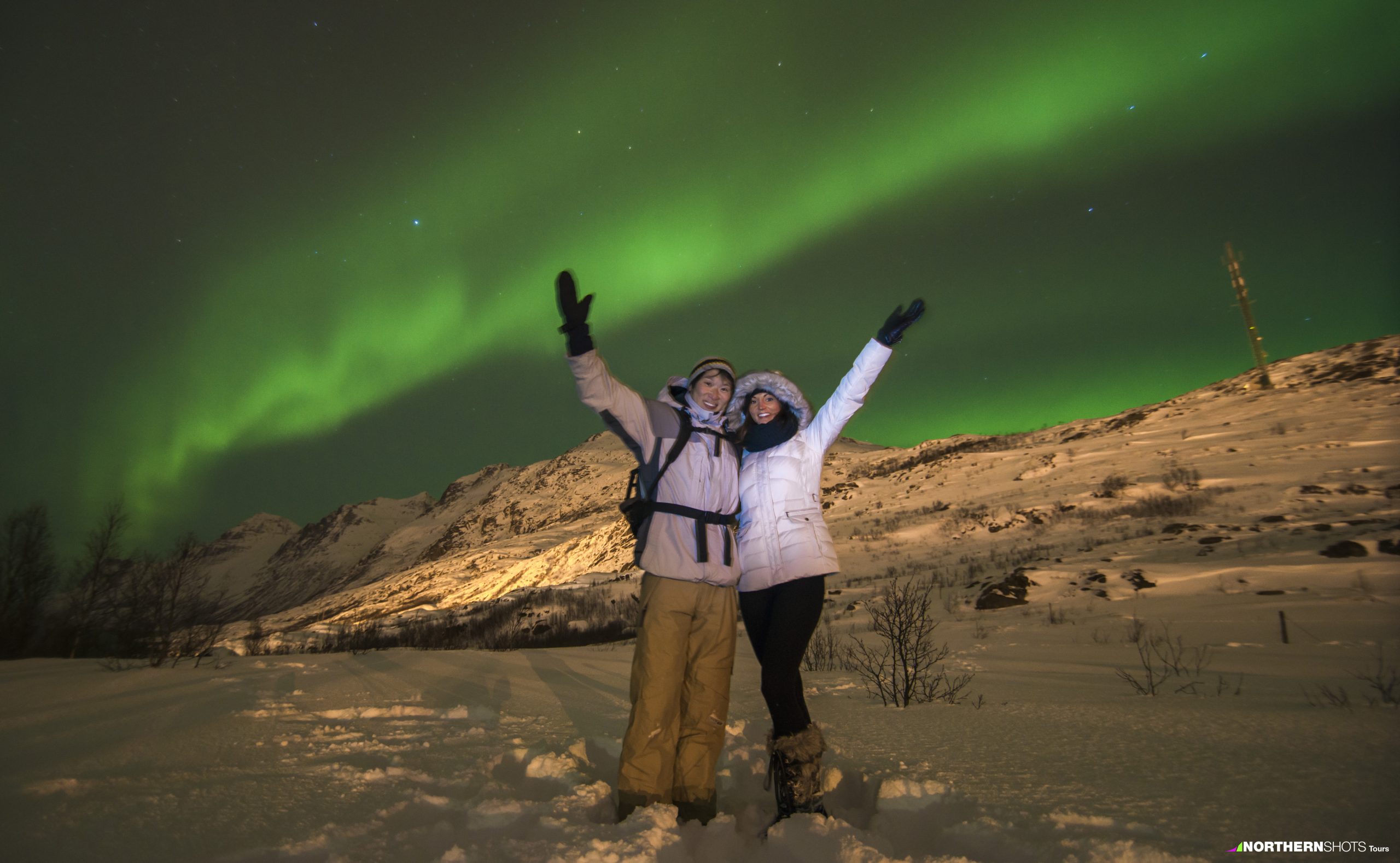 A man and woman under the green Aurora Borealis in Tromsø, Norway