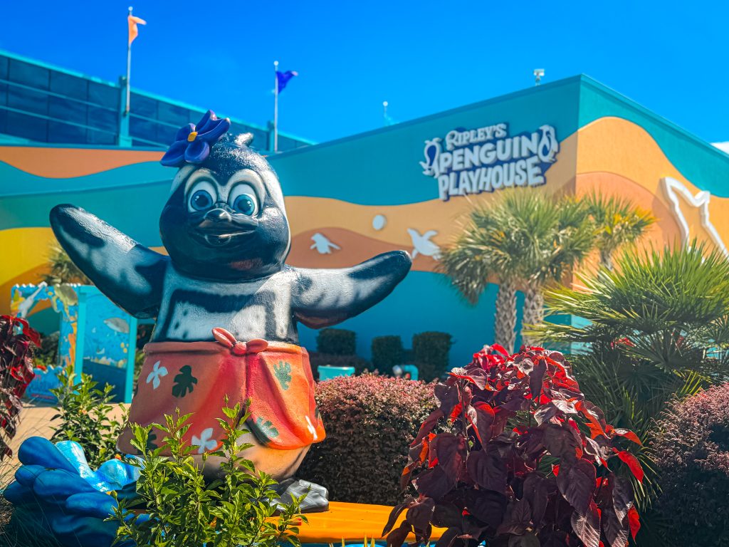 Statue of cartoon penguin wearing a flower and wrap skirt in front of colorful Ripley's aquarium