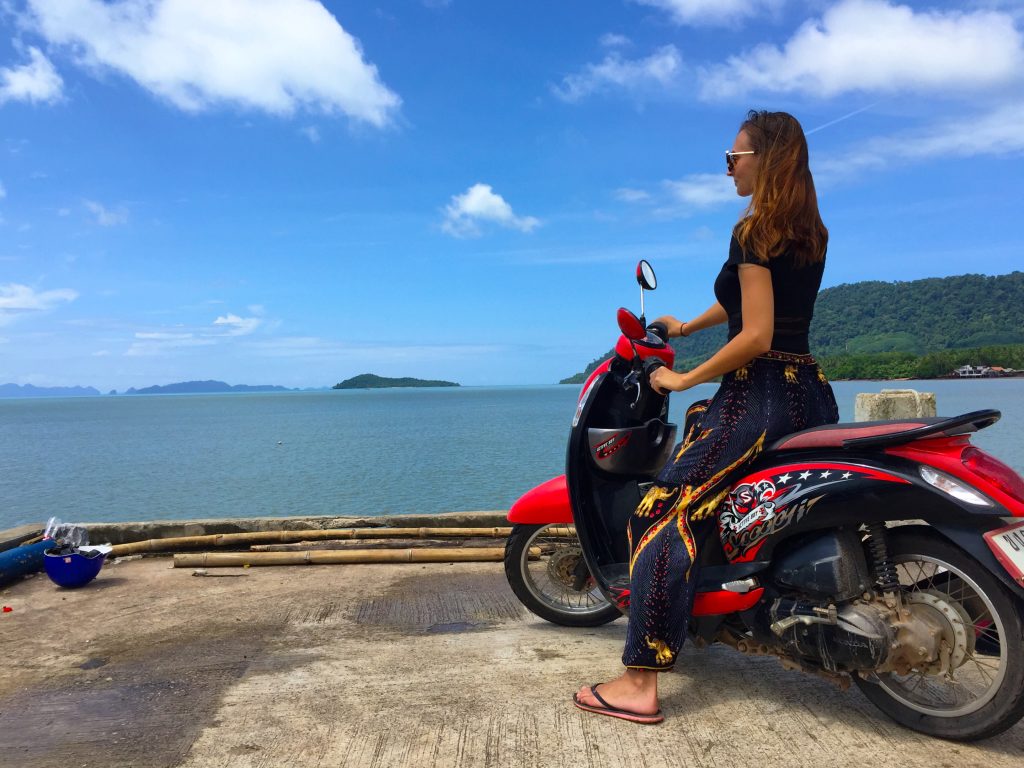Woman on a red scooter in front of the sea in Thailand