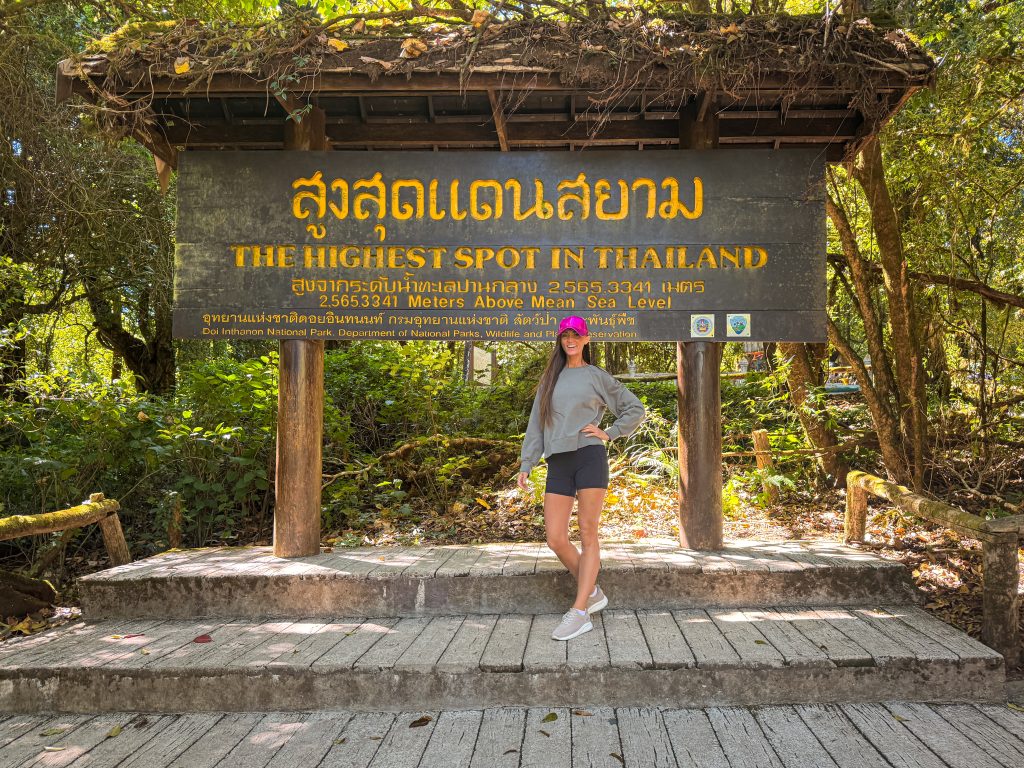 A woman in front of a sign for the highest spot in Thailand