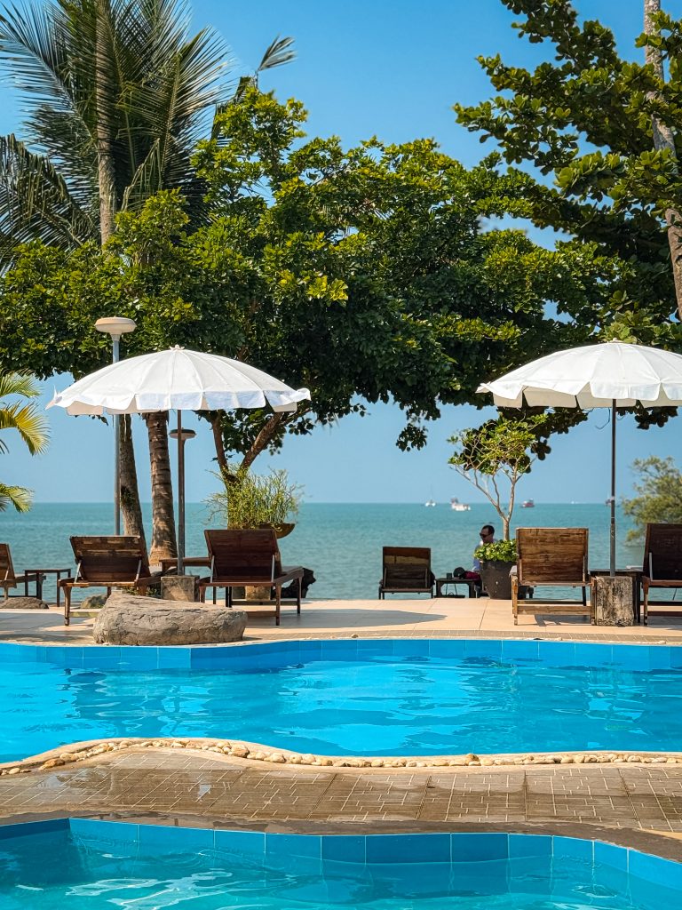 2 pools lined with beach chairs and trees in front of the sea in Thailand