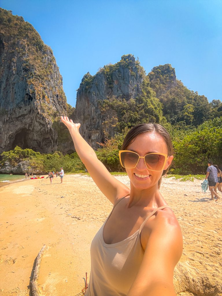 Smiling woman on a beach with hand outstretched towards dramatic limestone cliffs