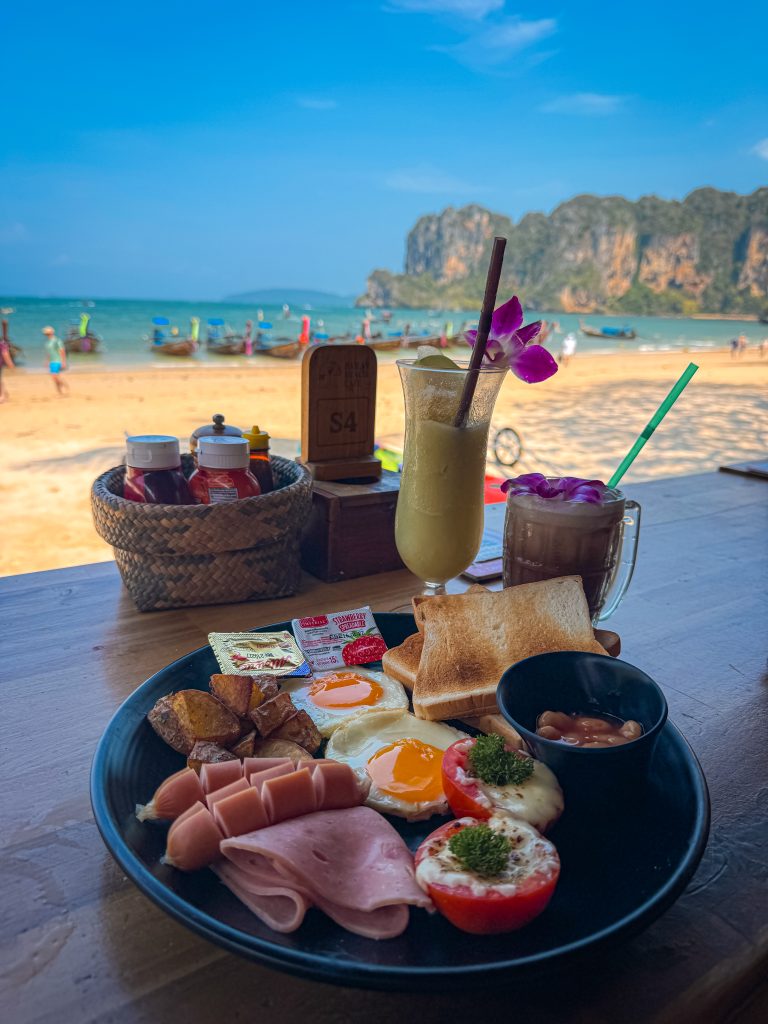 Breakfast plate with coffee and a smoothie with beach and limestone cliffs behind
