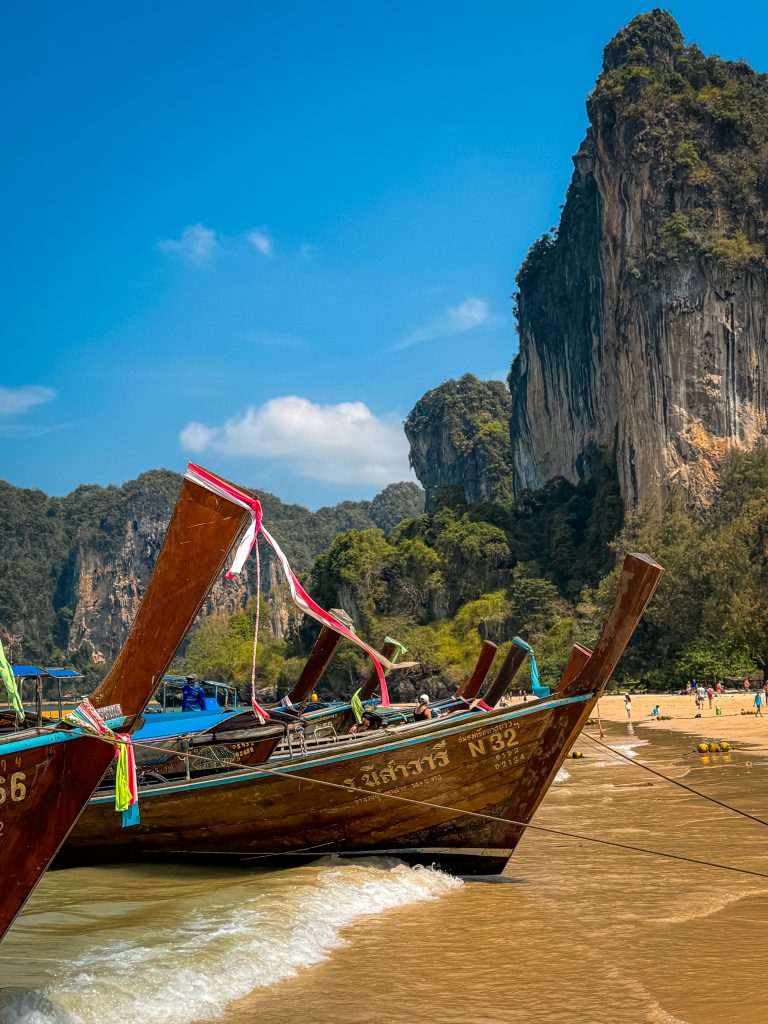 Wooden longtail boat on beach in Thailand in front of limestone cliff