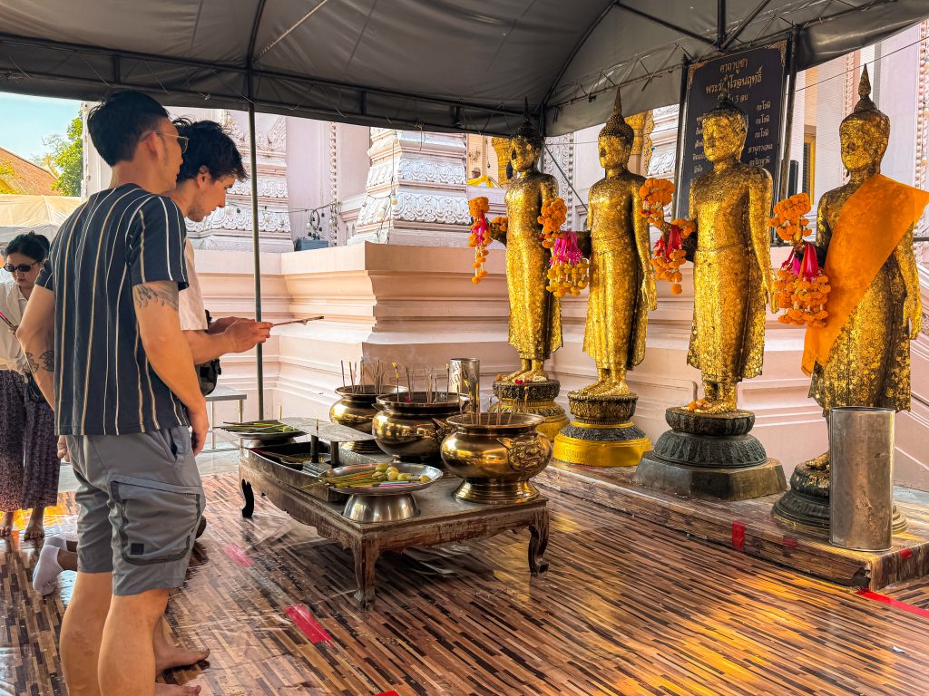 People giving offerings in front of golden buddha statues
