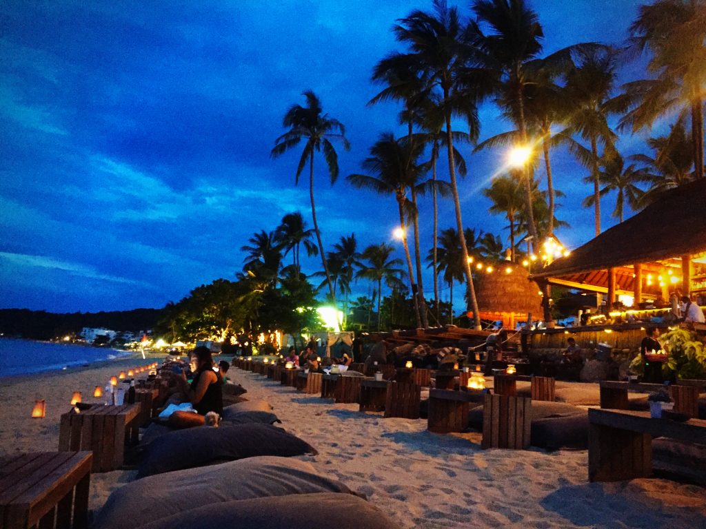 Bean bags and tables on the beach at twilight with palm trees and beach bar