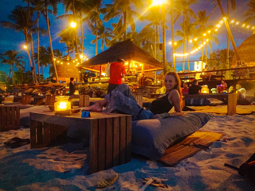 Woman sitting on a bean bag at lit up beach bar