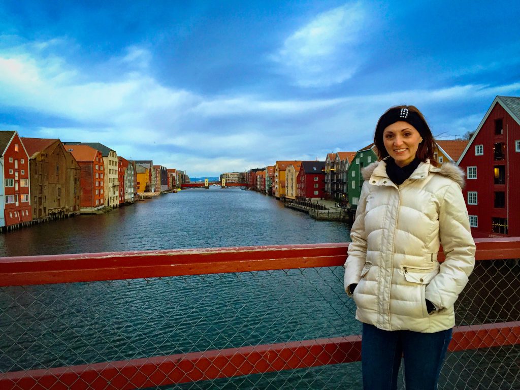 Woman in a winter jacket in front of colorful riverfront houses in Trondheim, Norway