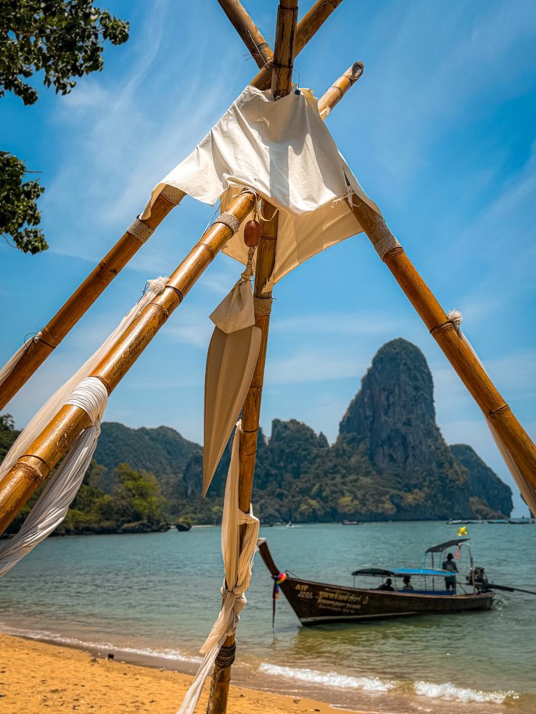 Bamboo structure framing a longtail boat with limestone cliff behind