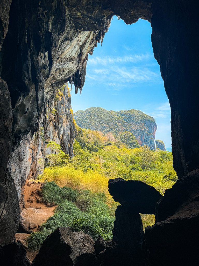 View through a large Bat Cave opening toward the forest and limestone cliffs of Railay.