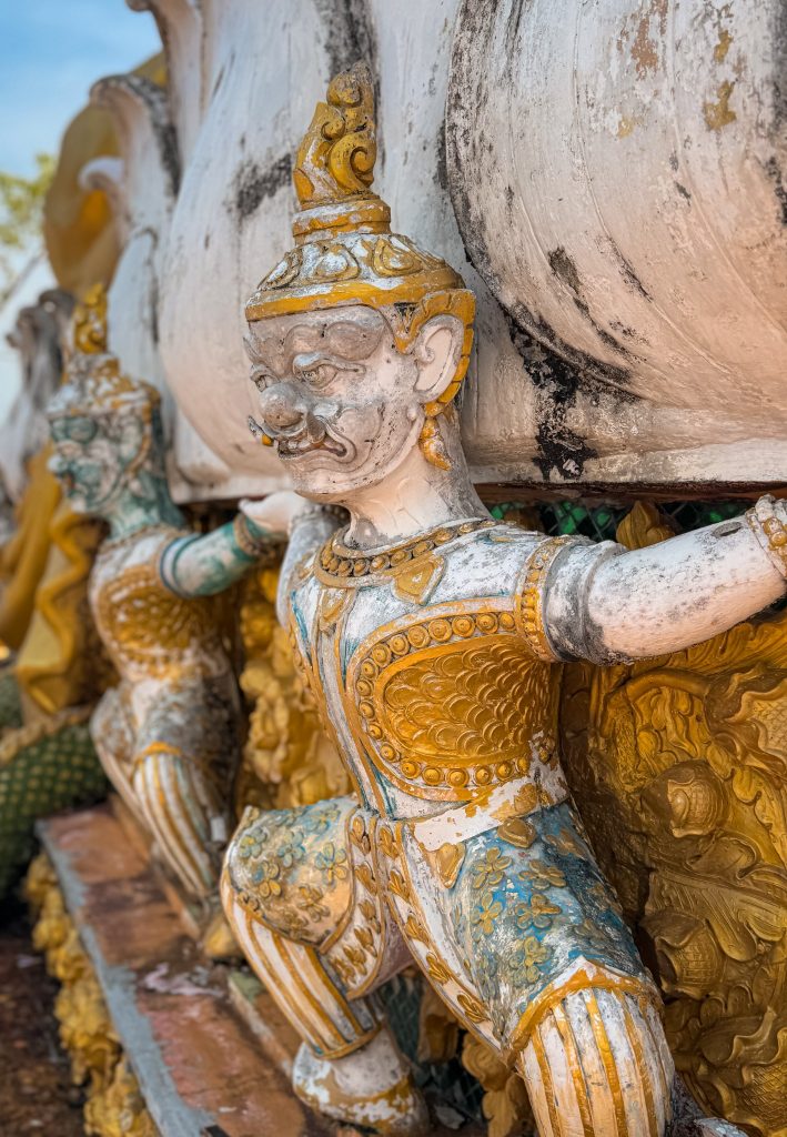 Weathered guardian statue supporting a structure at Tiger Cave Temple